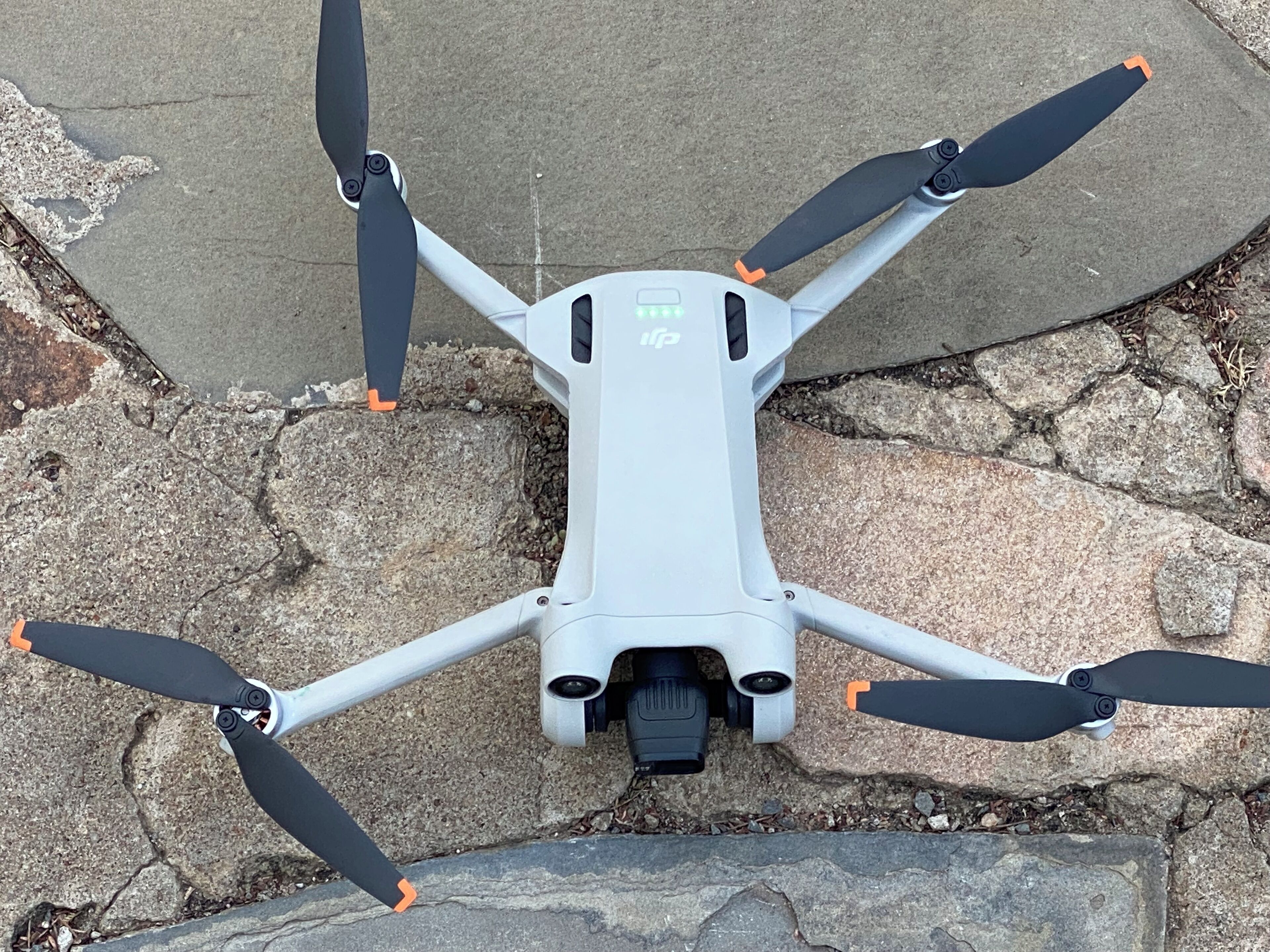A drone with four propellers and a camera mounted on a white body with orange accents.