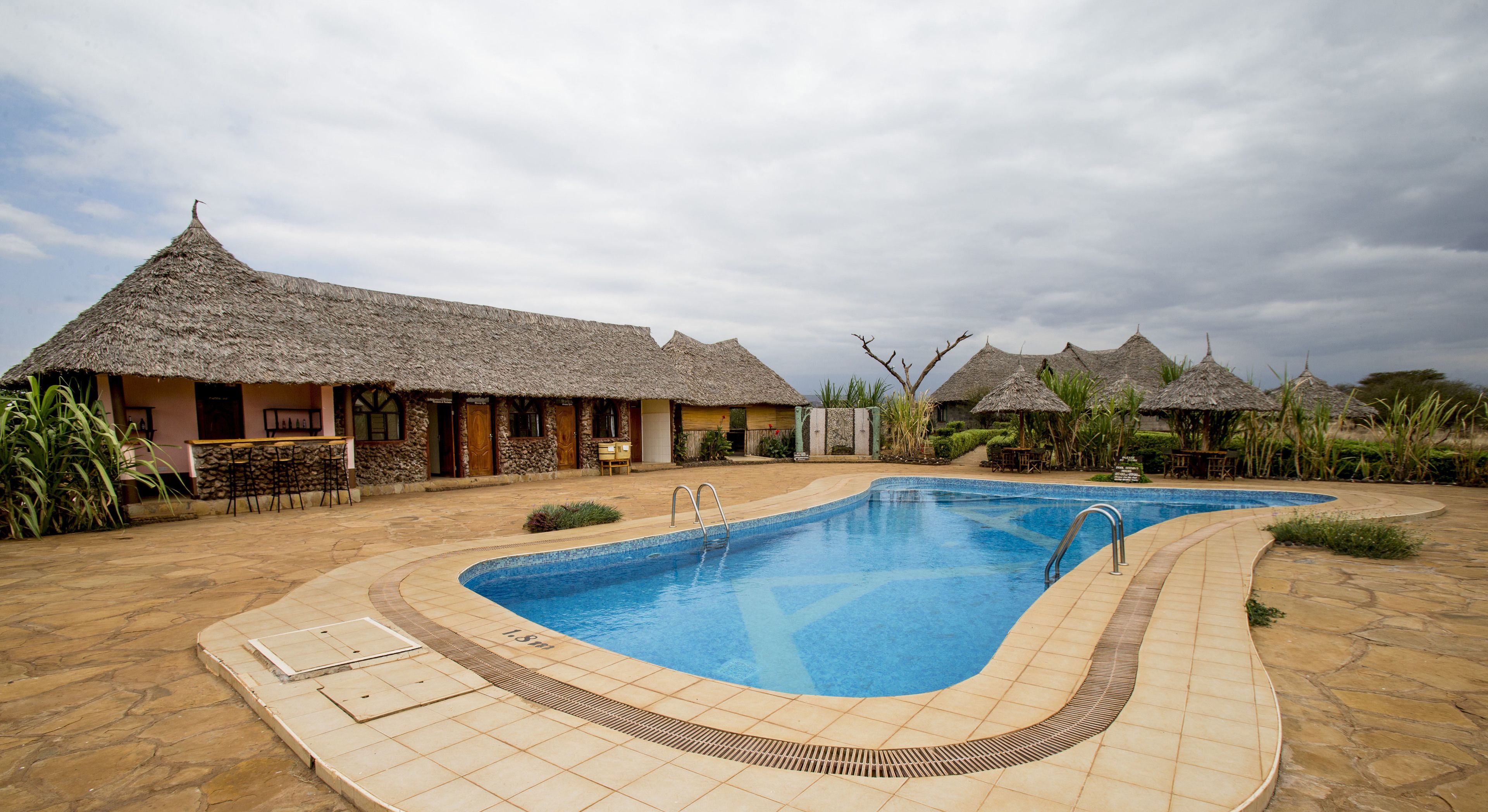 A pool area with a thatched-roof building, a stone pathway, and a bar area.