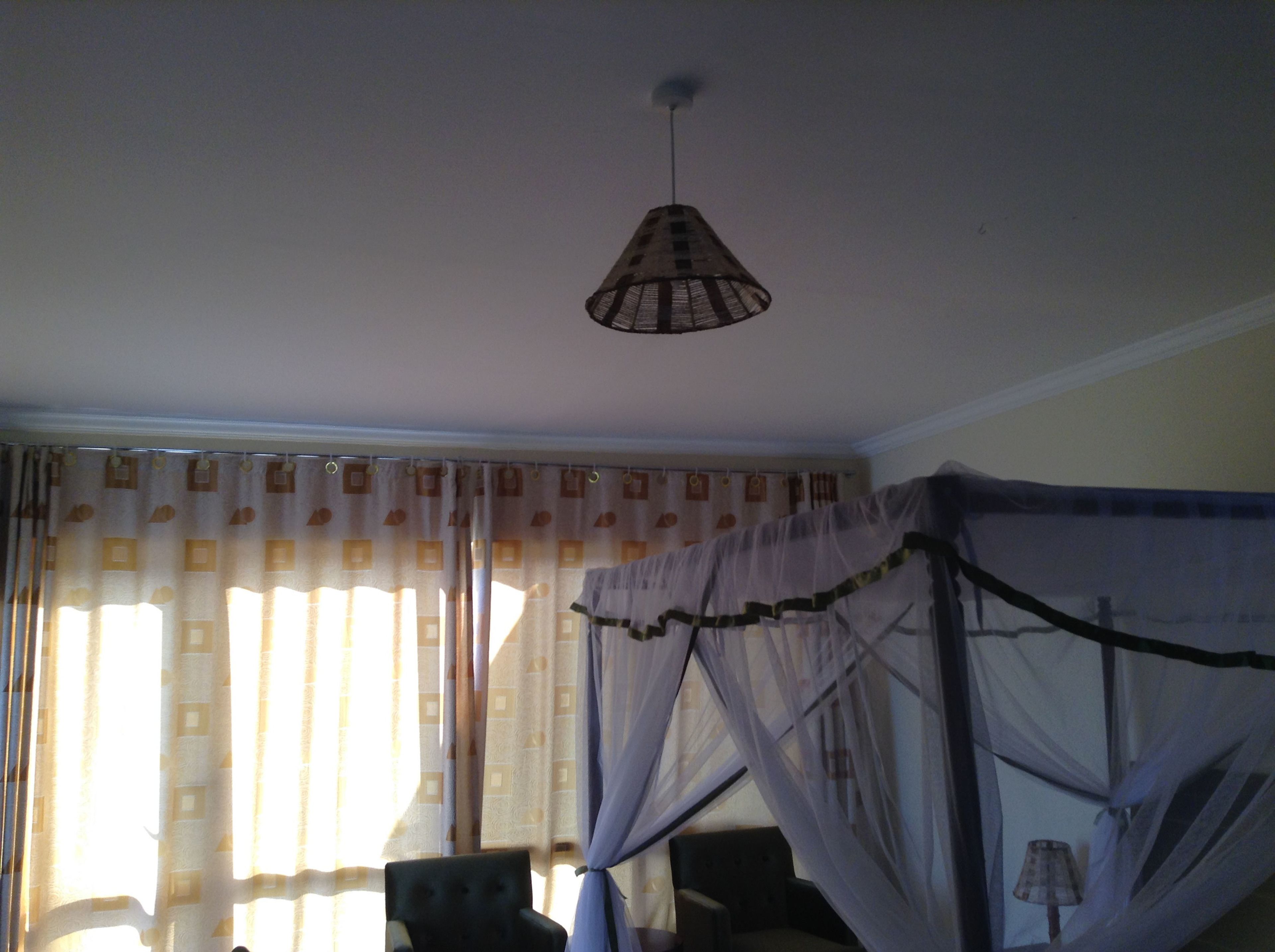 A room with a bed covered in mosquito netting, a hanging lamp, and curtains with a geometric pattern.