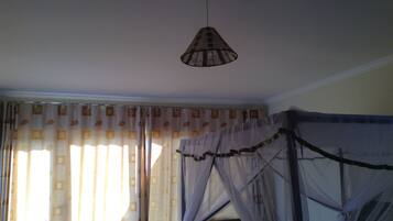 A room with a bed covered in mosquito netting, a hanging lamp, and curtains with a geometric pattern.