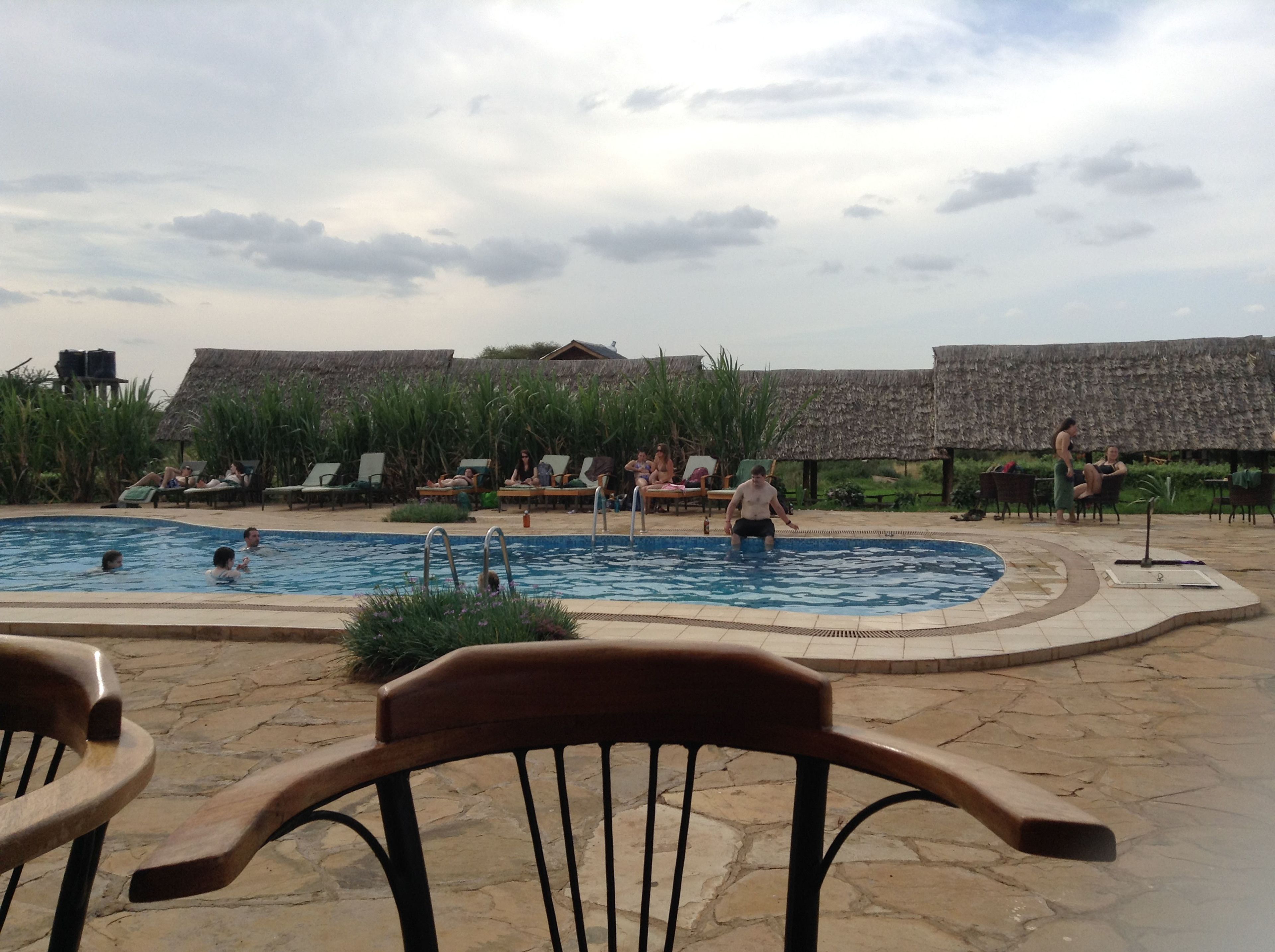 Un área de piscina con sillas de descanso y sombrillas, rodeada de construcciones con techo de paja.