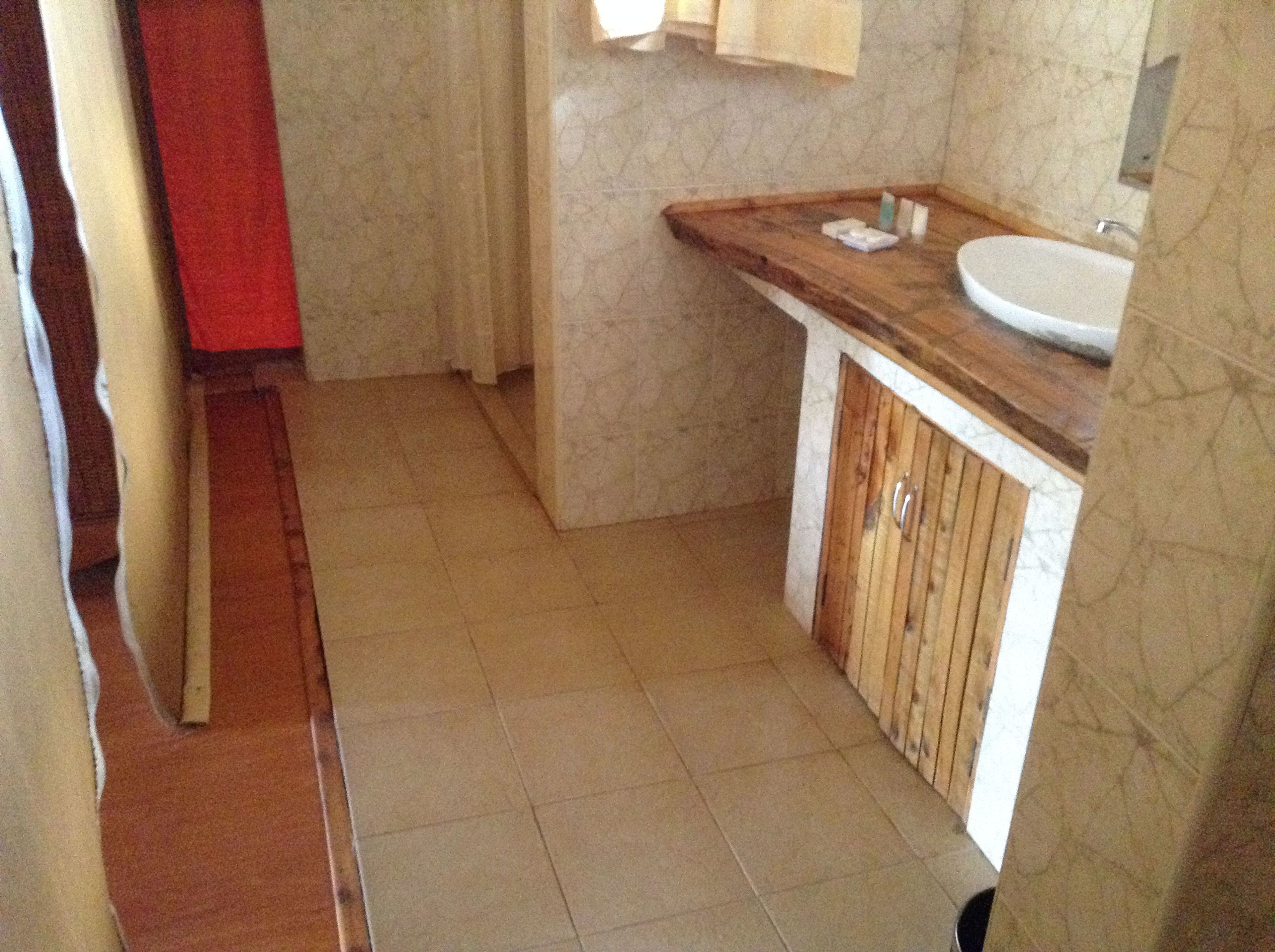 Un baño pequeño con un tocador de madera, un lavamanos blanco y suelo de baldosas.