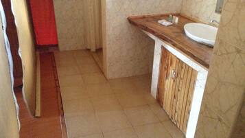Un baño pequeño con un tocador de madera, un lavamanos blanco y suelo de baldosas.