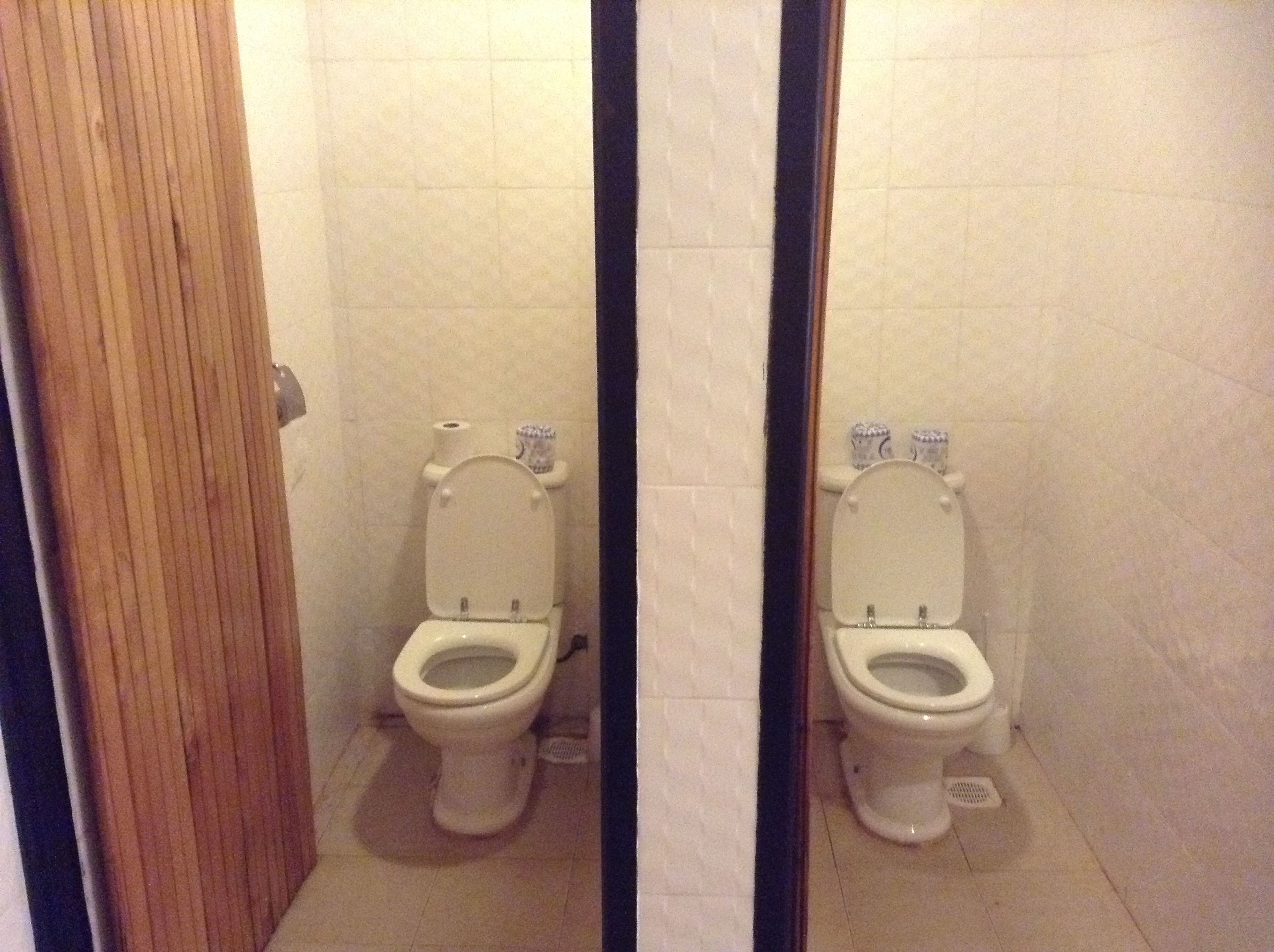 A standard bathroom with two toilets, tiled walls, and a wooden door.