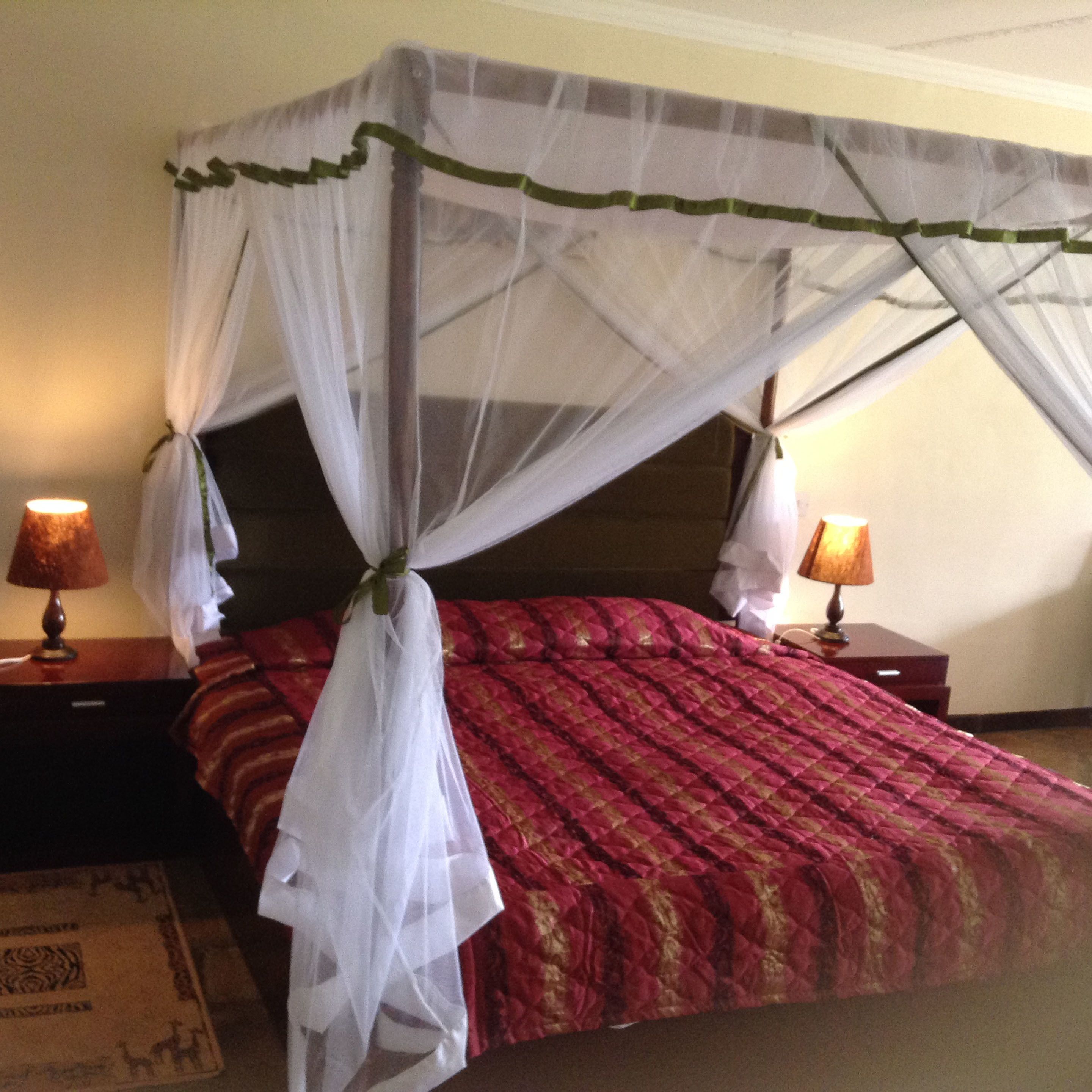 A bed with a canopy, two bedside lamps, and a patterned rug.