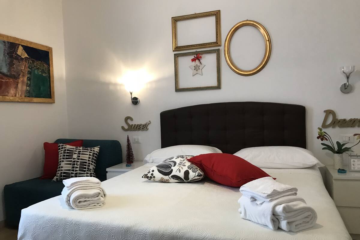A neatly made bed with white linens, a dark headboard, and a small Christmas tree on the nightstand.