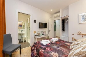 A hotel room with a bed, a desk, a television, a wardrobe, and a bathroom visible through an open door. - St. Peter's Relax (Rome)