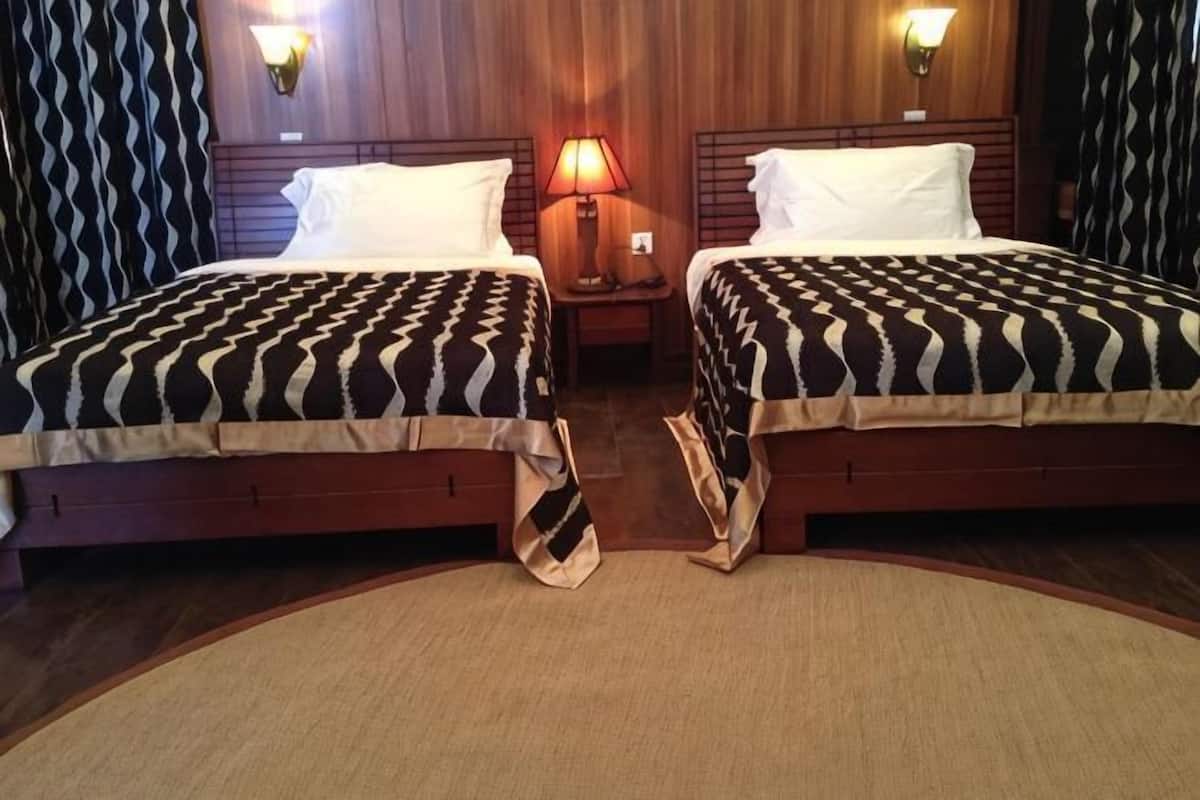 Una habitación de hotel con dos camas, cabeceros de madera, una mesita de noche con lámpara y una alfombra.