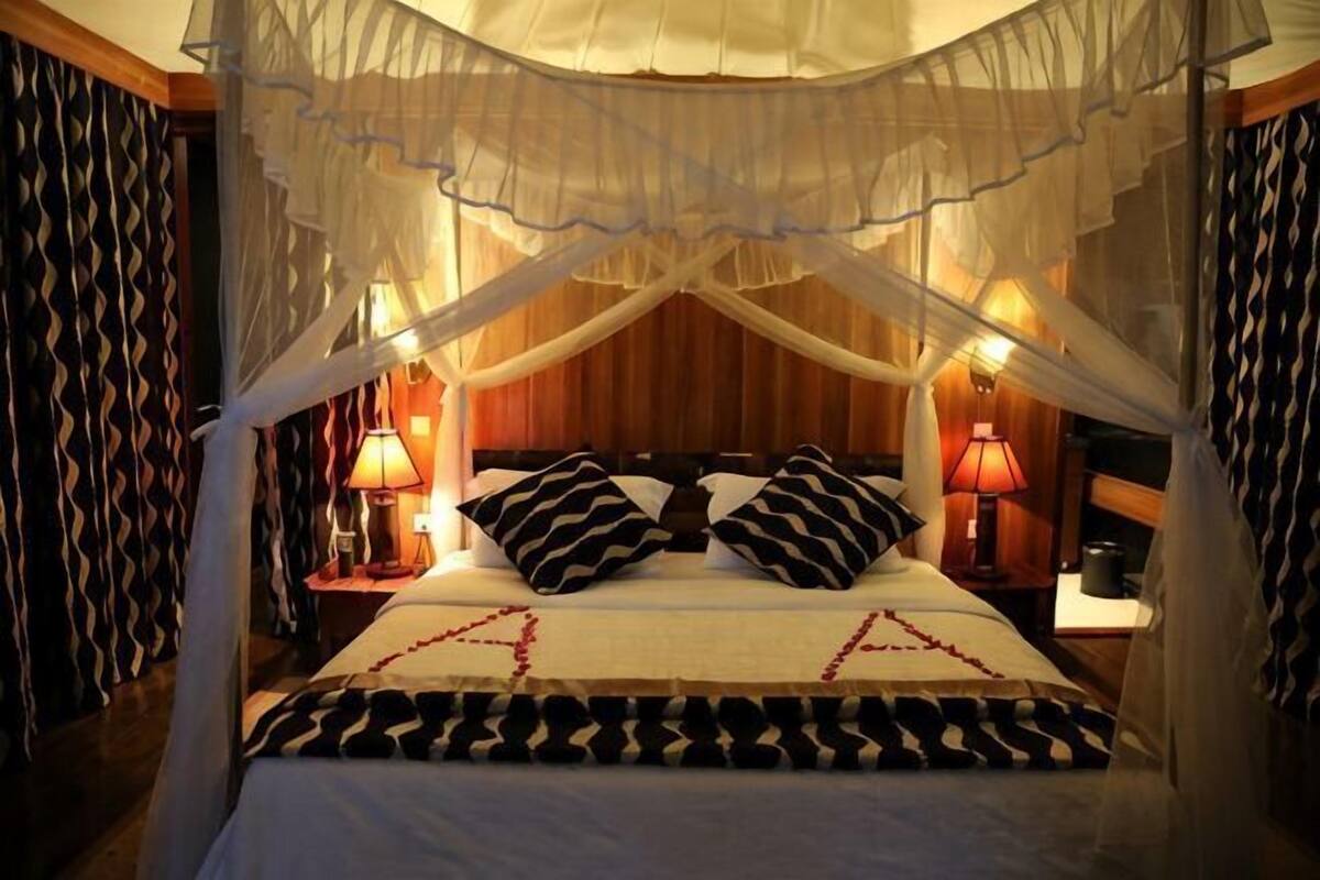 Una cama con dosel, dos mesitas de noche con lámparas, ropa de cama estampada y un cabecero de madera.