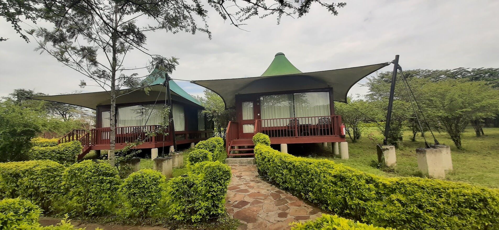 Dos cabañas para huéspedes con un sendero que conduce a la entrada principal, rodeadas de setos y árboles bien cuidados.