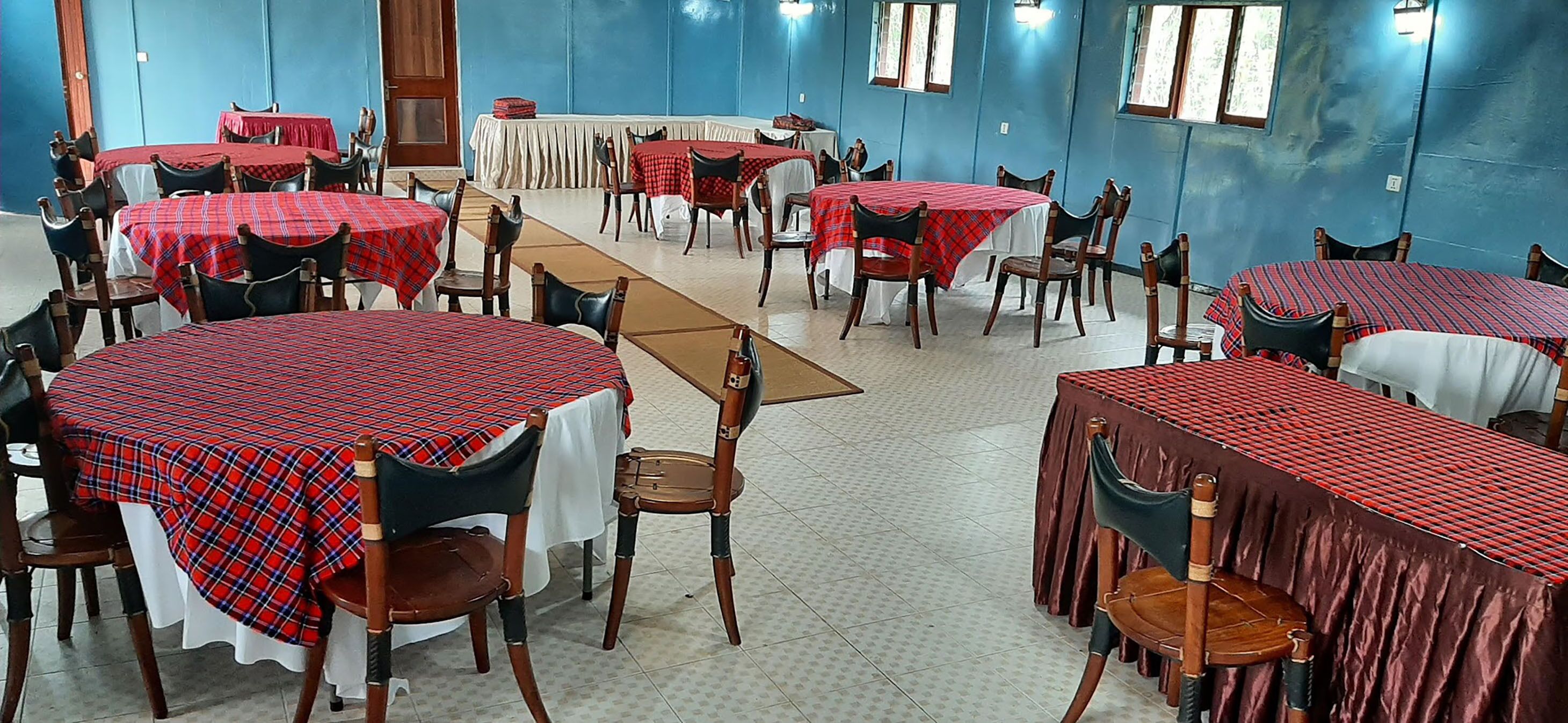 A dining area with tables covered in red and white checkered tablecloths, wooden chairs, and blue walls.