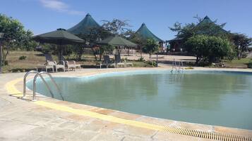 Relax by the serene pool surrounded by lounge chairs and umbrellas, under a shaded gazebo.