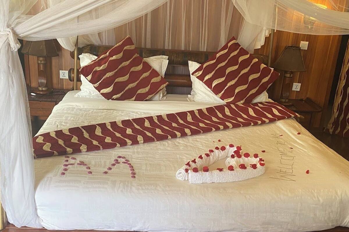 Una cama con dosel, varias almohadas, una toalla con diseño de corazón y un cartel que dice "WELCOME".