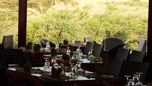 Un restaurant dont les tables sont dressées pour le service, avec des nappes à carreaux et des chaises noires, et qui offre une vue sur un paysage naturel composé d’arbres et de collines.