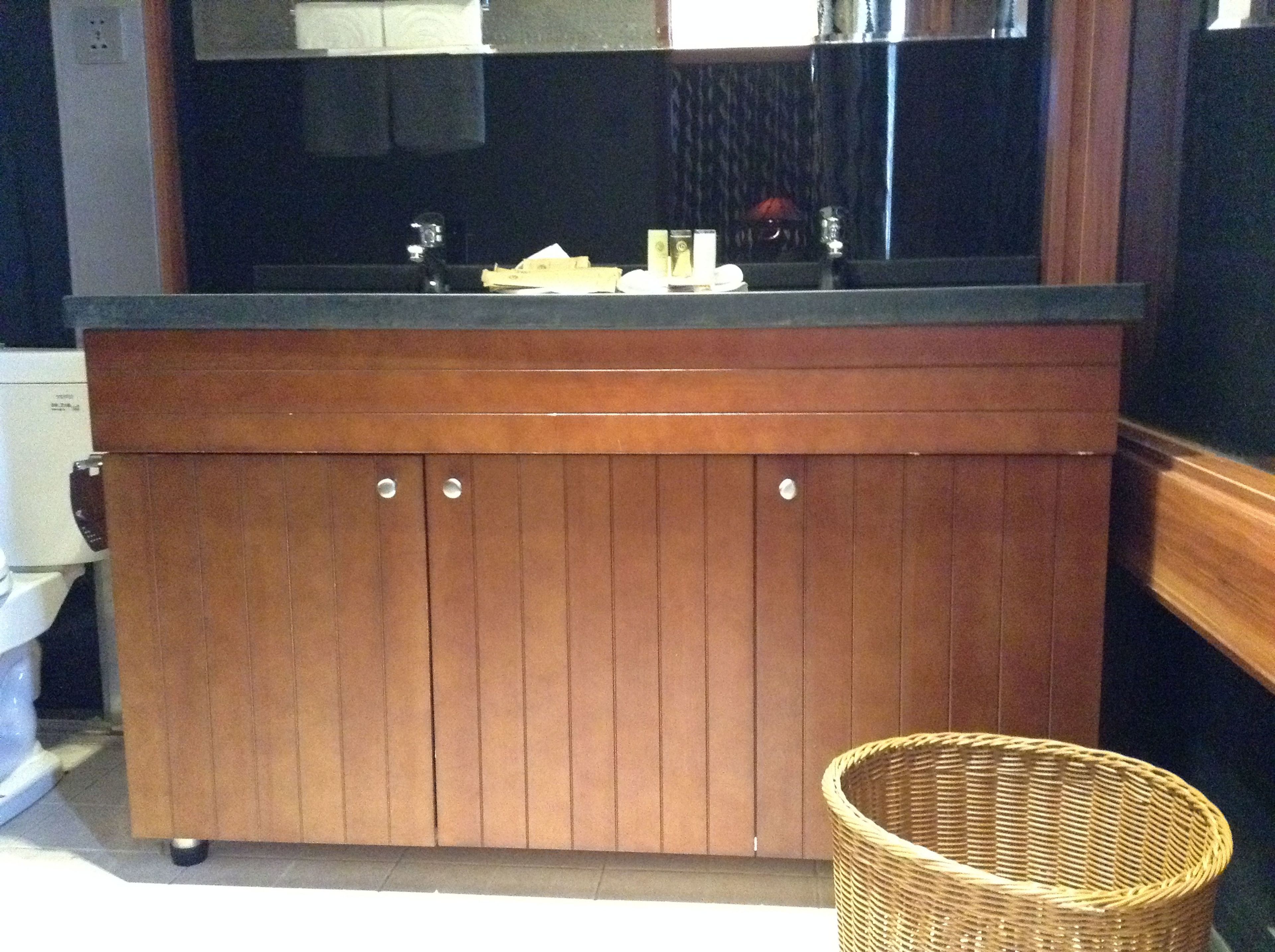 Una cocina de madera con encimera negra, un fregadero y armarios. Hay una cesta de mimbre en el suelo.