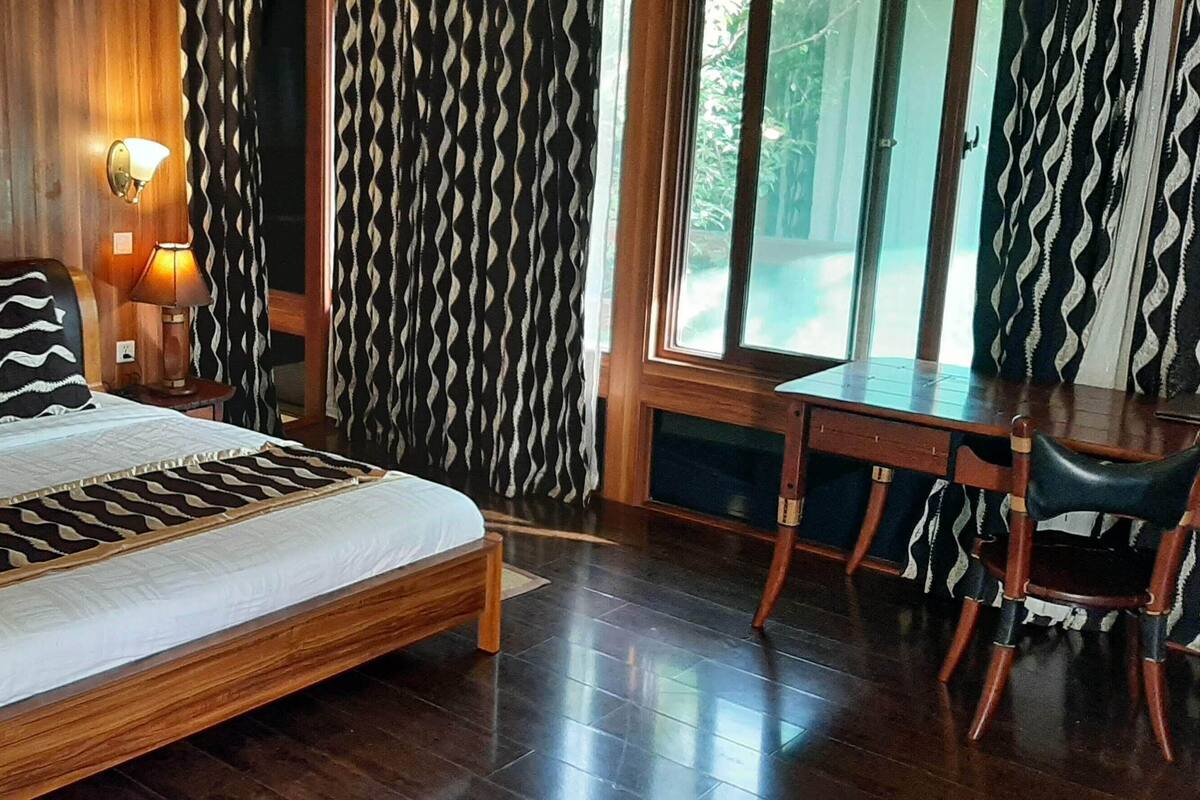 Una cama de madera con almohadas estampadas, un escritorio con una silla y una ventana con cortinas.