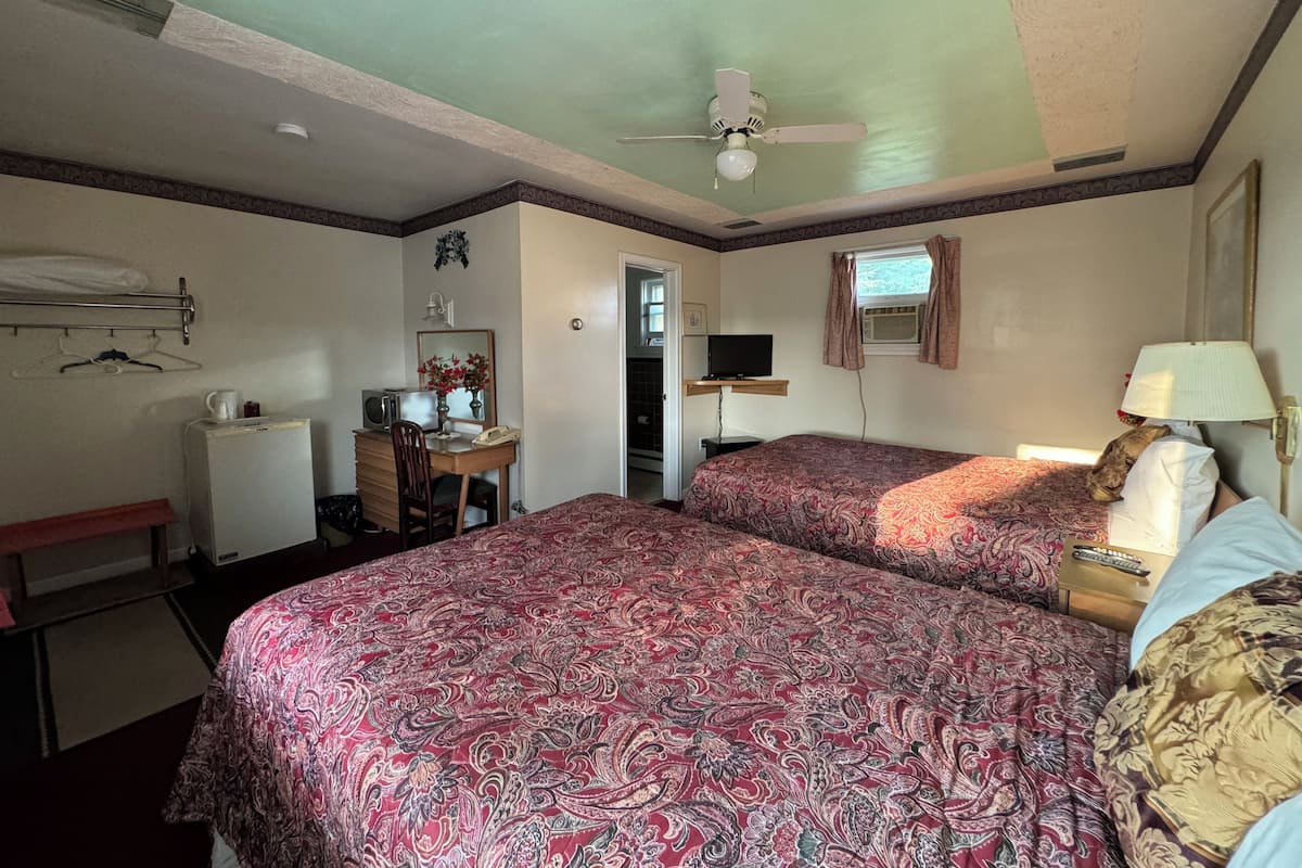A hotel room with two beds, a desk with a chair, a television, and a ceiling fan.