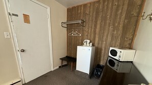 Habitación pequeña con pared de madera, un refrigerador, un microondas, un teléfono y un perchero con ganchos.