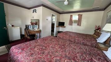 A hotel room with two beds, a desk with a chair, a television, and a ceiling fan.