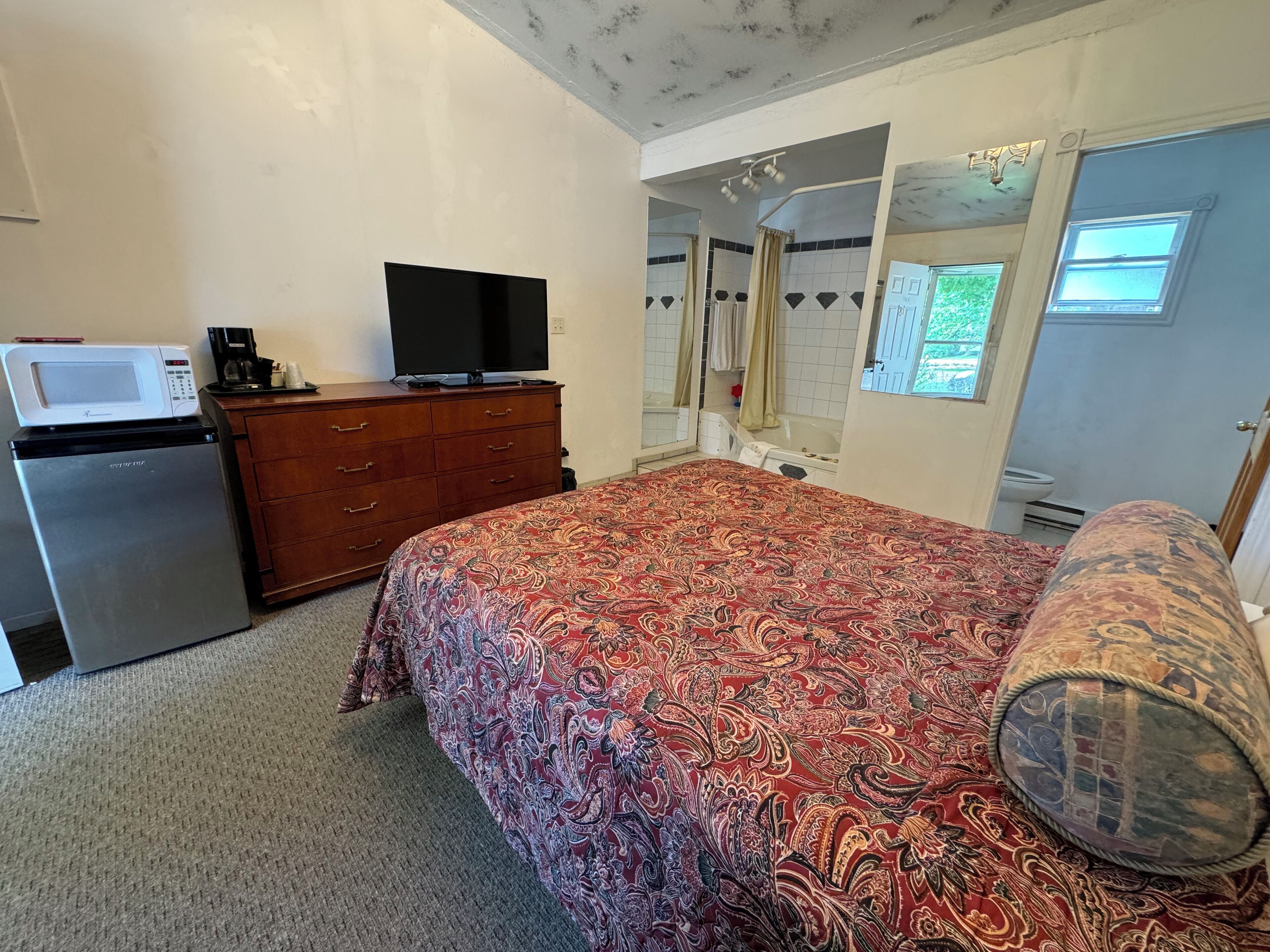 Un dormitorio con cama, cómoda, microondas, televisión y baño visible a través de una puerta abierta.