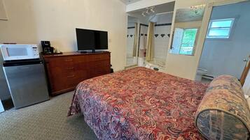 Un dormitorio con cama, cómoda, microondas, televisión y baño visible a través de una puerta abierta.