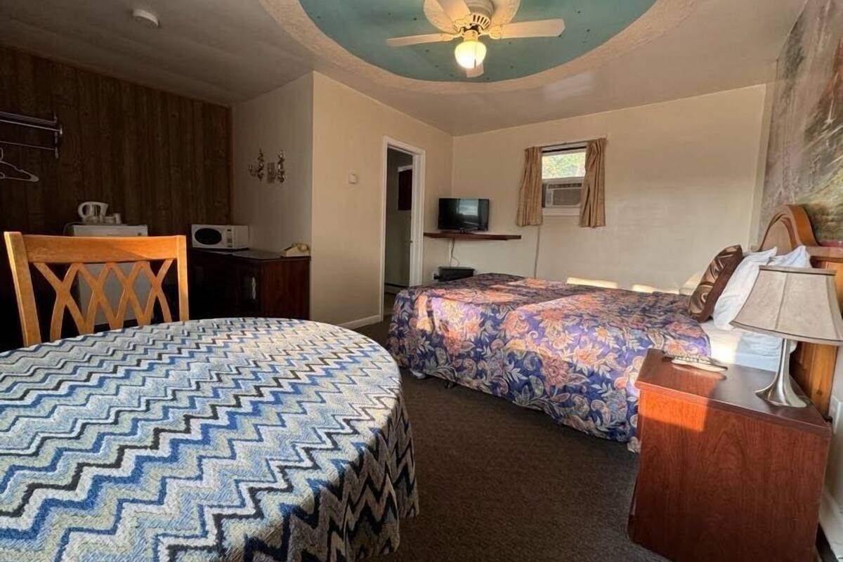 A room with a bed, a chair, a desk, a television, and a ceiling fan.
