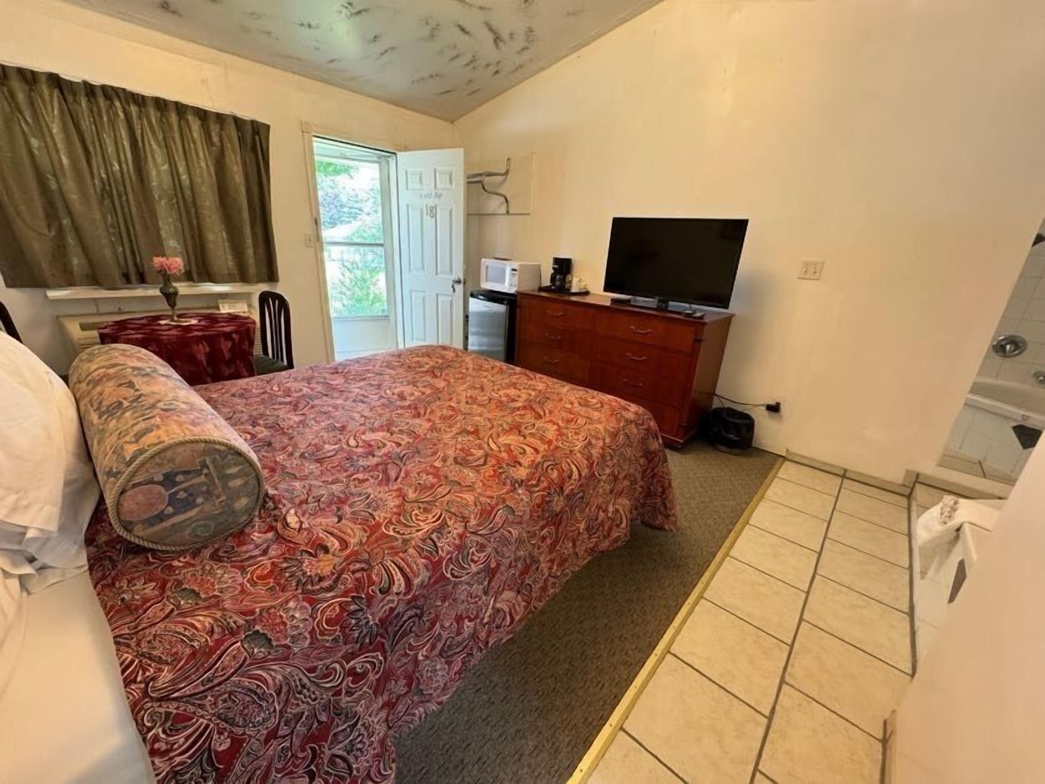Ein Schlafzimmer mit einem Bett, einem Schminktisch, einem Fernseher und einem Fenster mit Vorhängen.