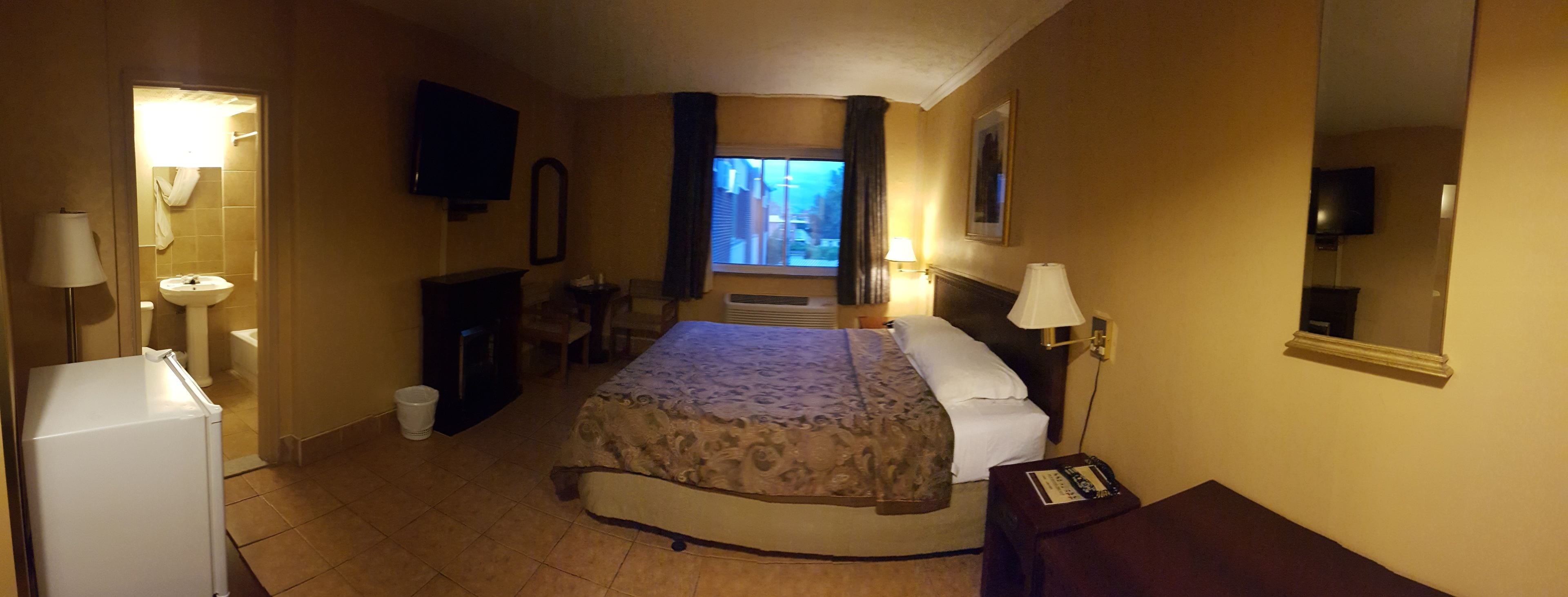 Une chambre d’hôtel comprenant un lit, des lampes de chevet, une télévision, une petite table, une chaise, une fenêtre et un réfrigérateur.