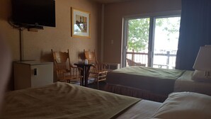 A hotel room with two beds, a desk, chairs, a TV, and a window with a view.