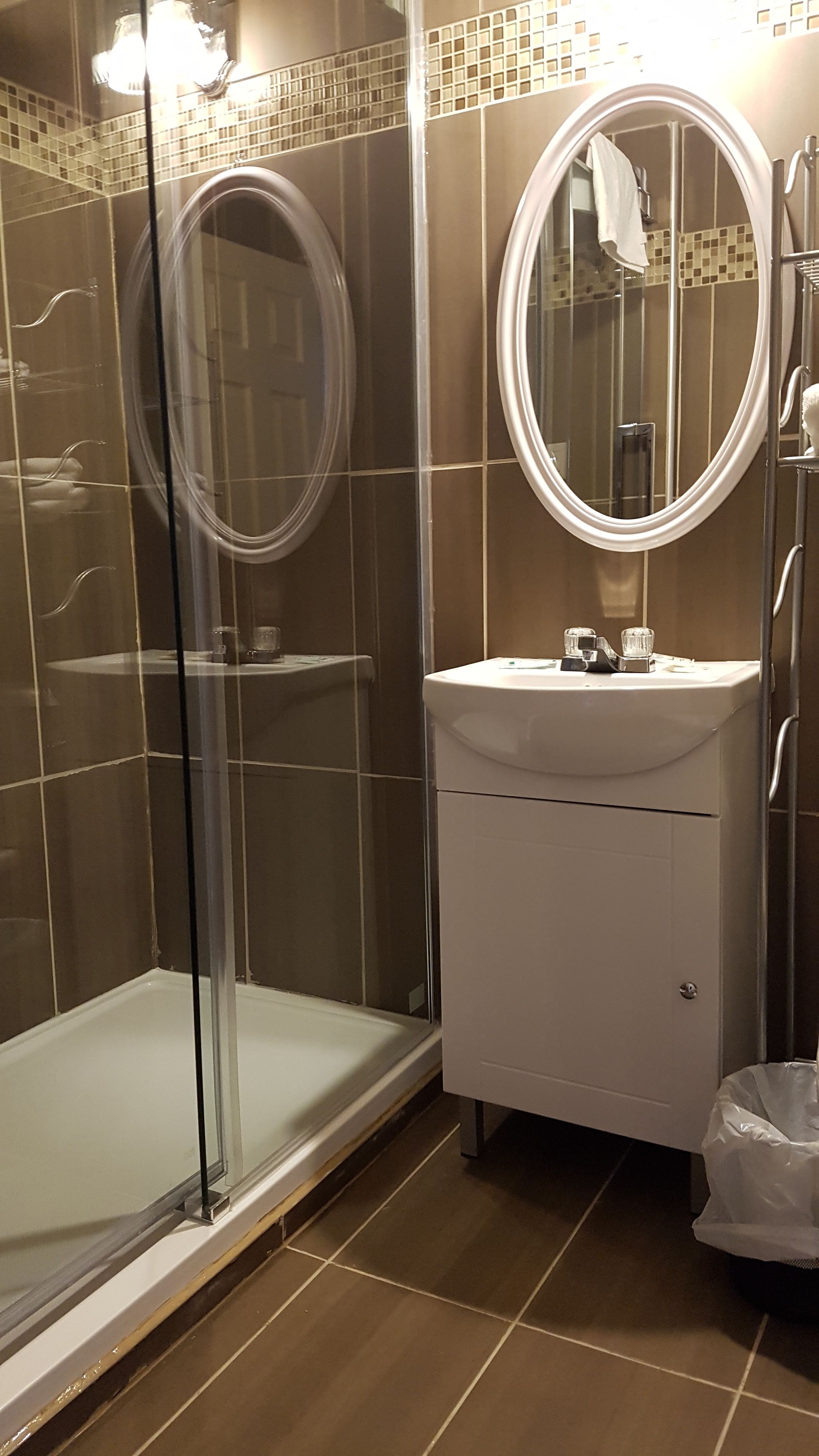 A bathroom with a glass-enclosed shower, a white sink with a mirror above it, and a tiled floor.