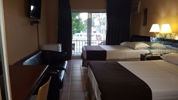 A hotel room with two beds, a desk, a chair, a TV, and a window with curtains.