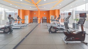 A gym with multiple cardio machines, including treadmills and an elliptical, with orange walls and a glass front.