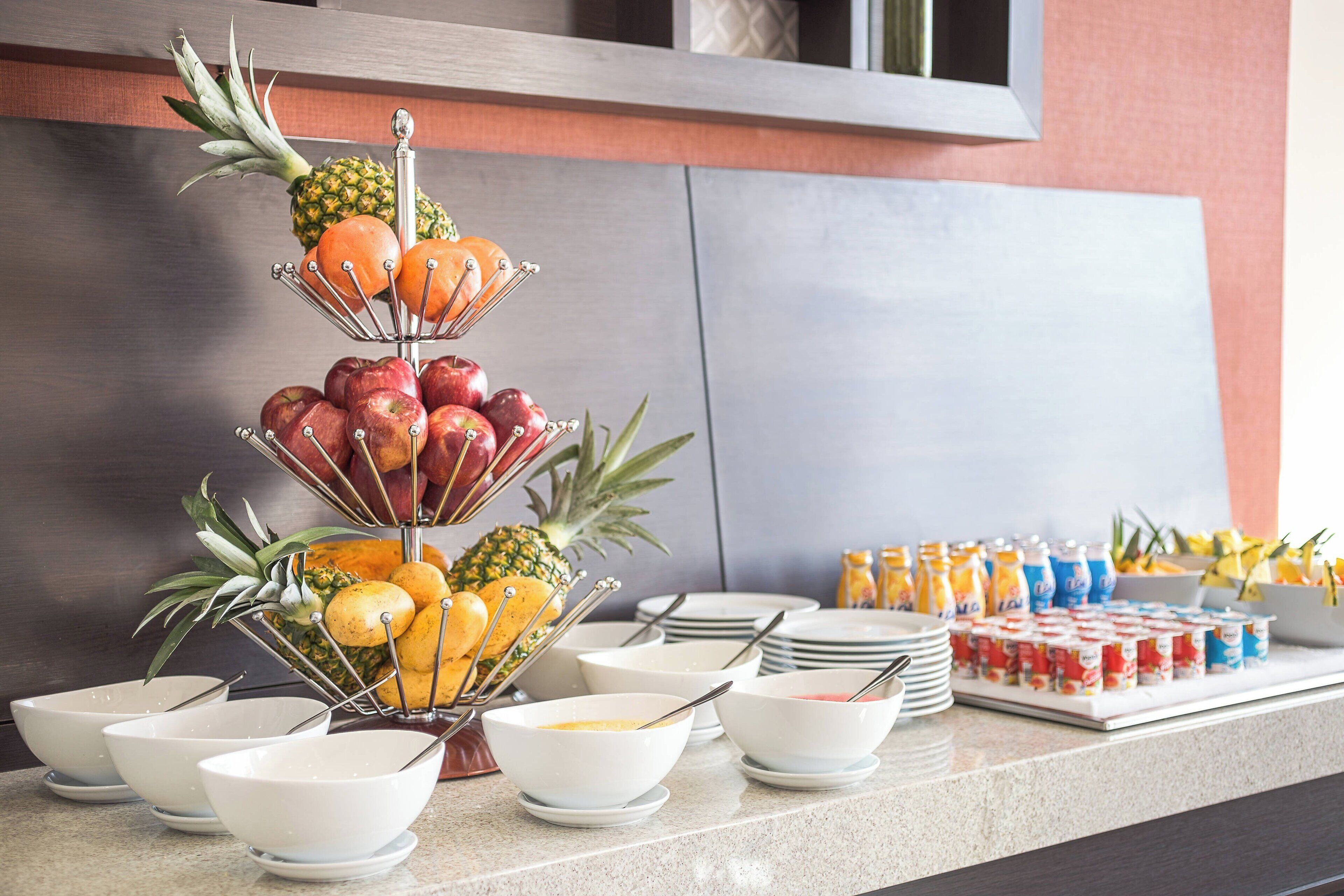 A buffet setup with a fruit display, bowls, and beverage containers.