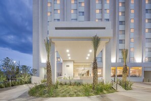 A modern hotel entrance with a covered walkway, palm trees, and a well-lit interior. - Courtyard by Marriott Saltillo (Saltillo)