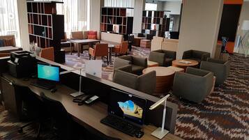 Uma biblioteca moderna com vários computadores, áreas de estar confortáveis e grandes janelas.