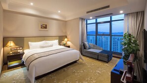 Habitación de hotel con una cama grande, un sofá, un escritorio y vistas a un paisaje urbano a través de la ventana.