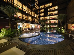 Een hotelatrium met een centraal gelegen zwembad, zitplaatsen binnen en een restaurant.