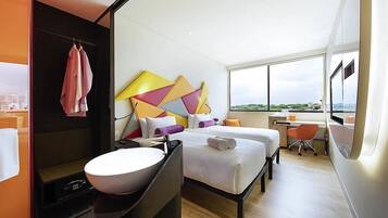 Habitación de hotel moderna con un ventanal grande, cama, escritorio y baño con lavamanos y espejo.