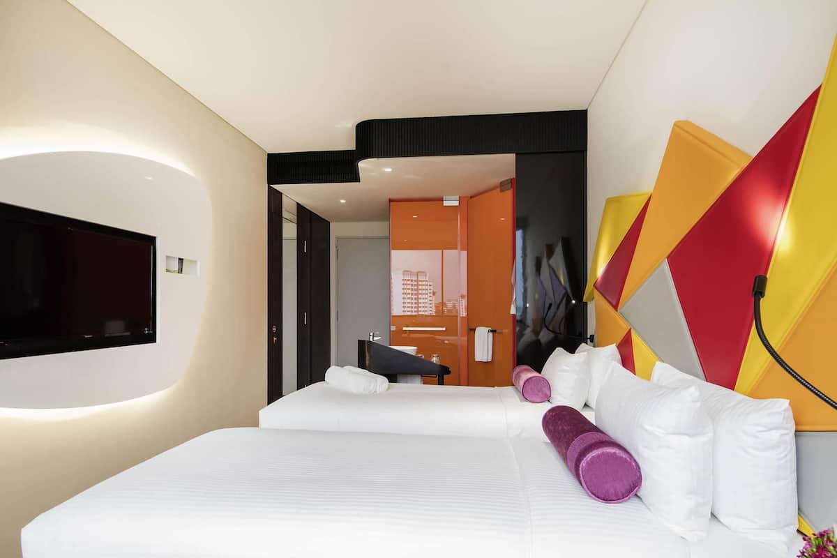 Een moderne hotelkamer met een groot bed, een flatscreen televisie aan de muur en uitzicht op de stad door de deur.