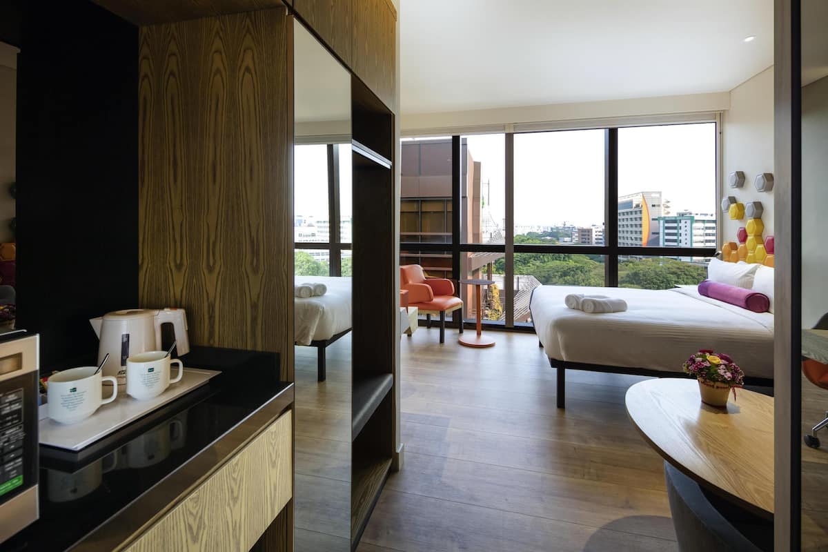 A modern hotel room with a large bed, a desk with a computer, a chair, and a view of the city.