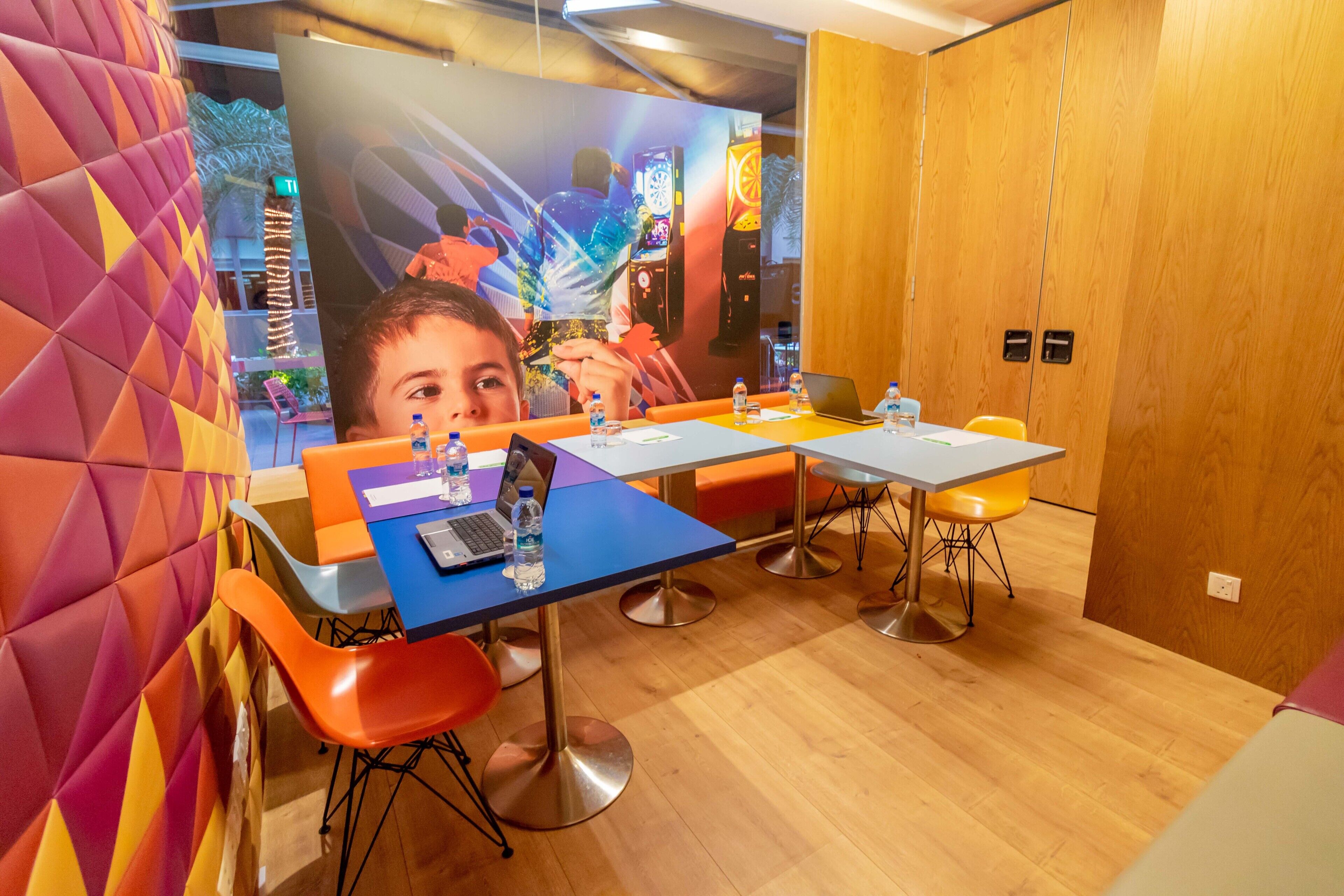 A modern conference room with a wooden floor, colorful walls, and orange and blue chairs.