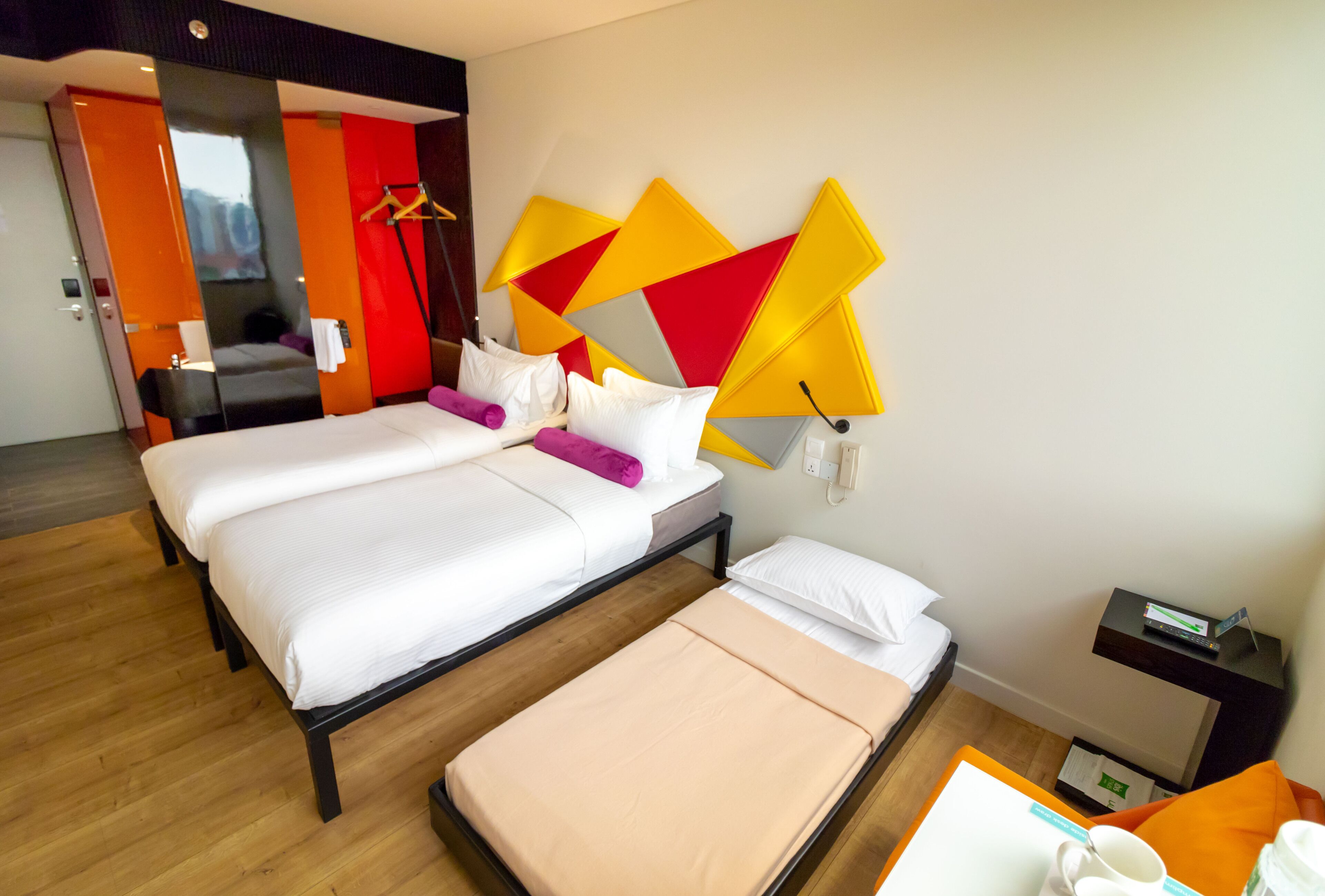 Ein Hotelzimmer mit zwei Betten, Holzboden, einem modernen Kopfteil und einem kleinen Tisch mit Tasse und Buch.