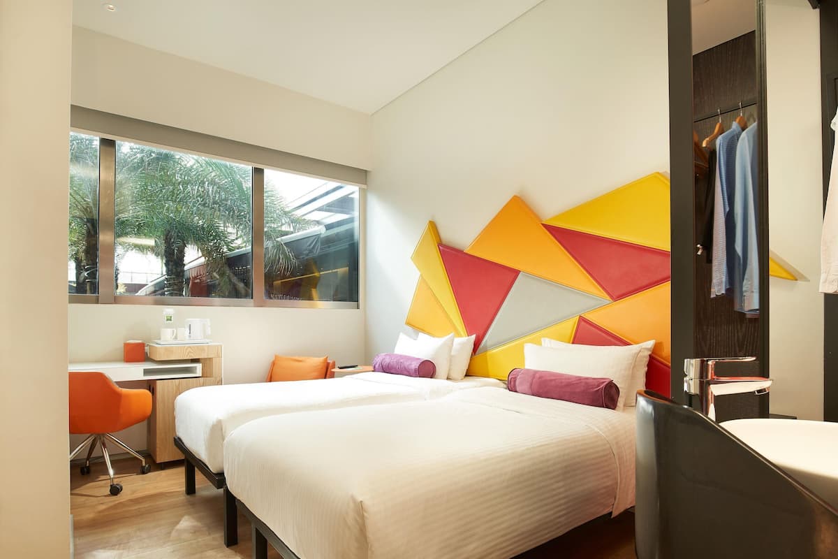 Een moderne hotelkamer met twee bedden, een bureau en een groot raam.