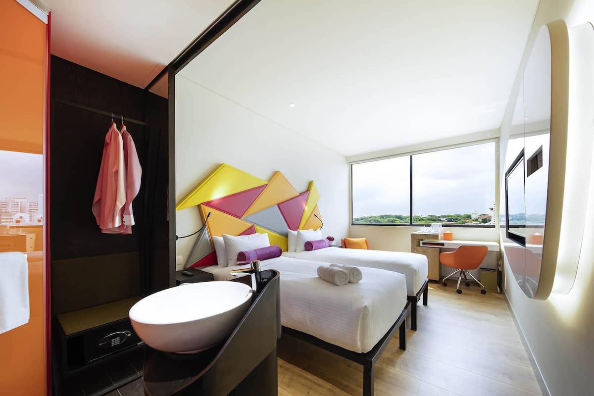 Een moderne hotelkamer met een groot bed, een bureau, een stoel, een badkamer met een wastafel en uitzicht op de stad.
