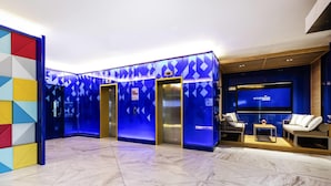 En moderne lobby med marmorgulv, elevatorer, et siddeområde med tv og en farverig geometrisk væg.
