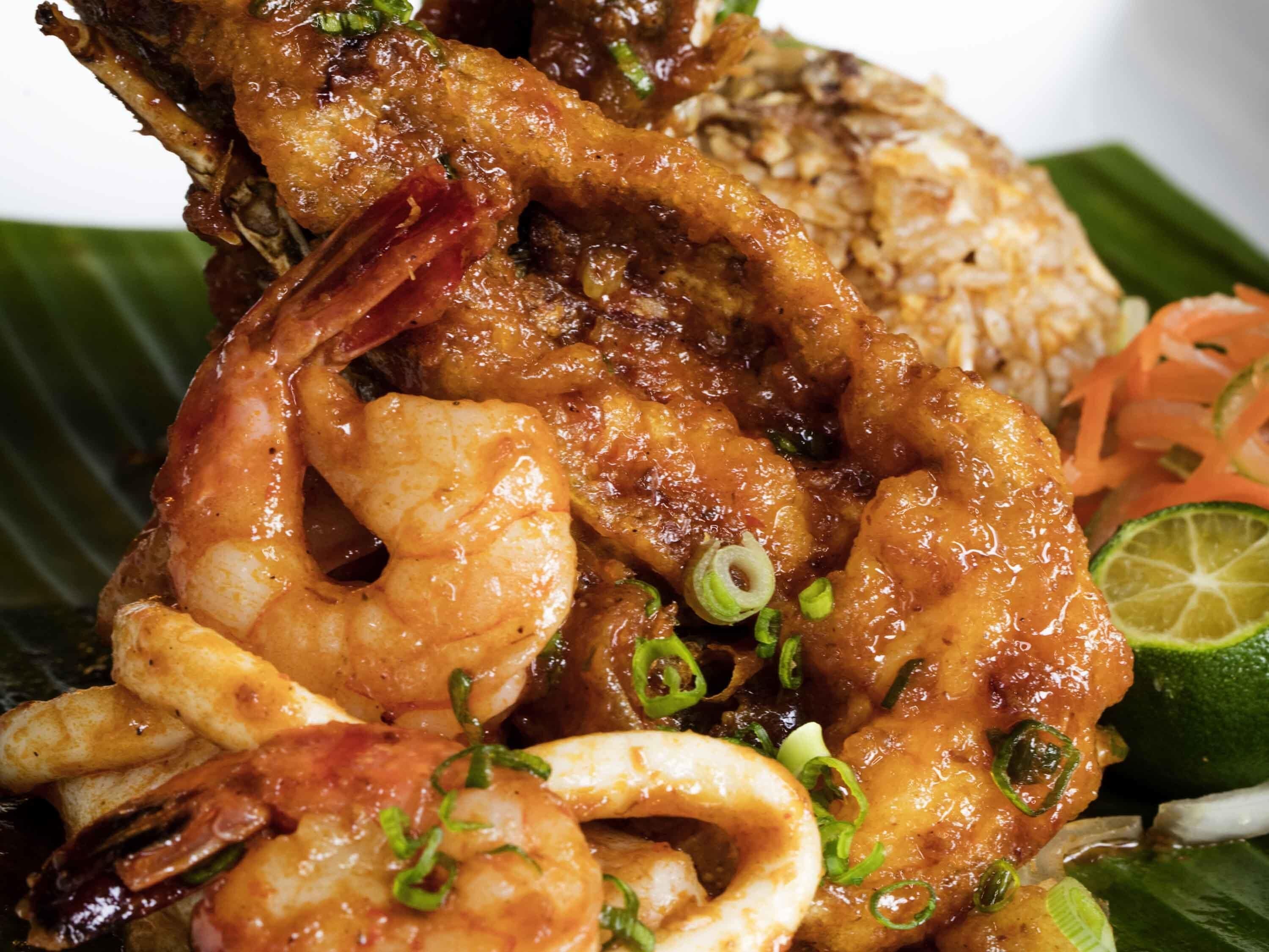 A seafood dish with shrimp, squid, and fish, garnished with green onions and served with rice and vegetables.