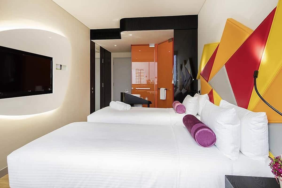 A modern hotel room with a large bed, a flat-screen TV mounted on the wall, and a distinctive geometric wall decoration.