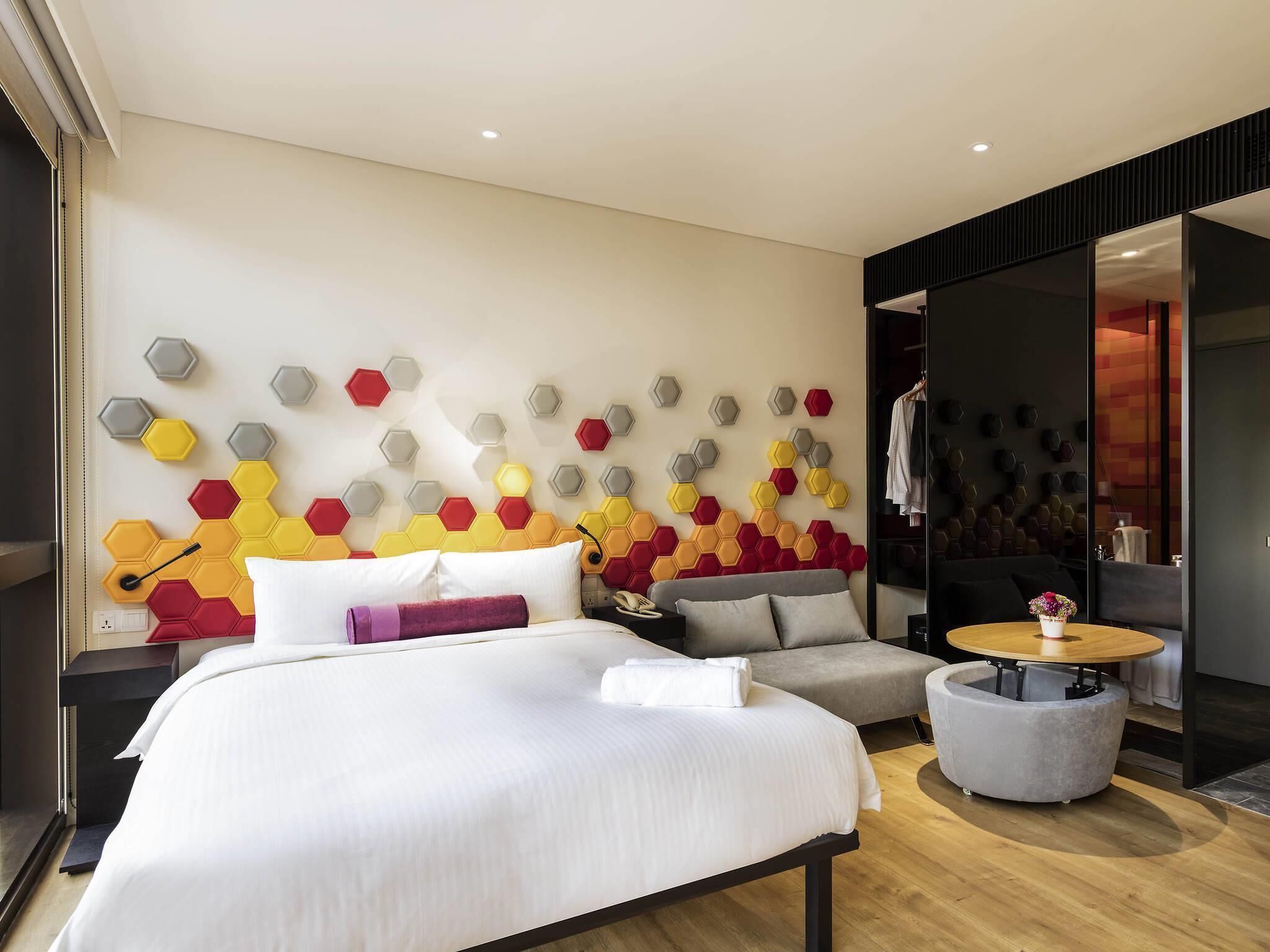 Een moderne hotelkamer met een groot bed, een ronde salontafel, een bank en een decoratieve wand met honingraatmotieven.