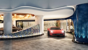En moderne lobby med en central trappe, en rød sportsvogn og en blå dekorativ søjle.
