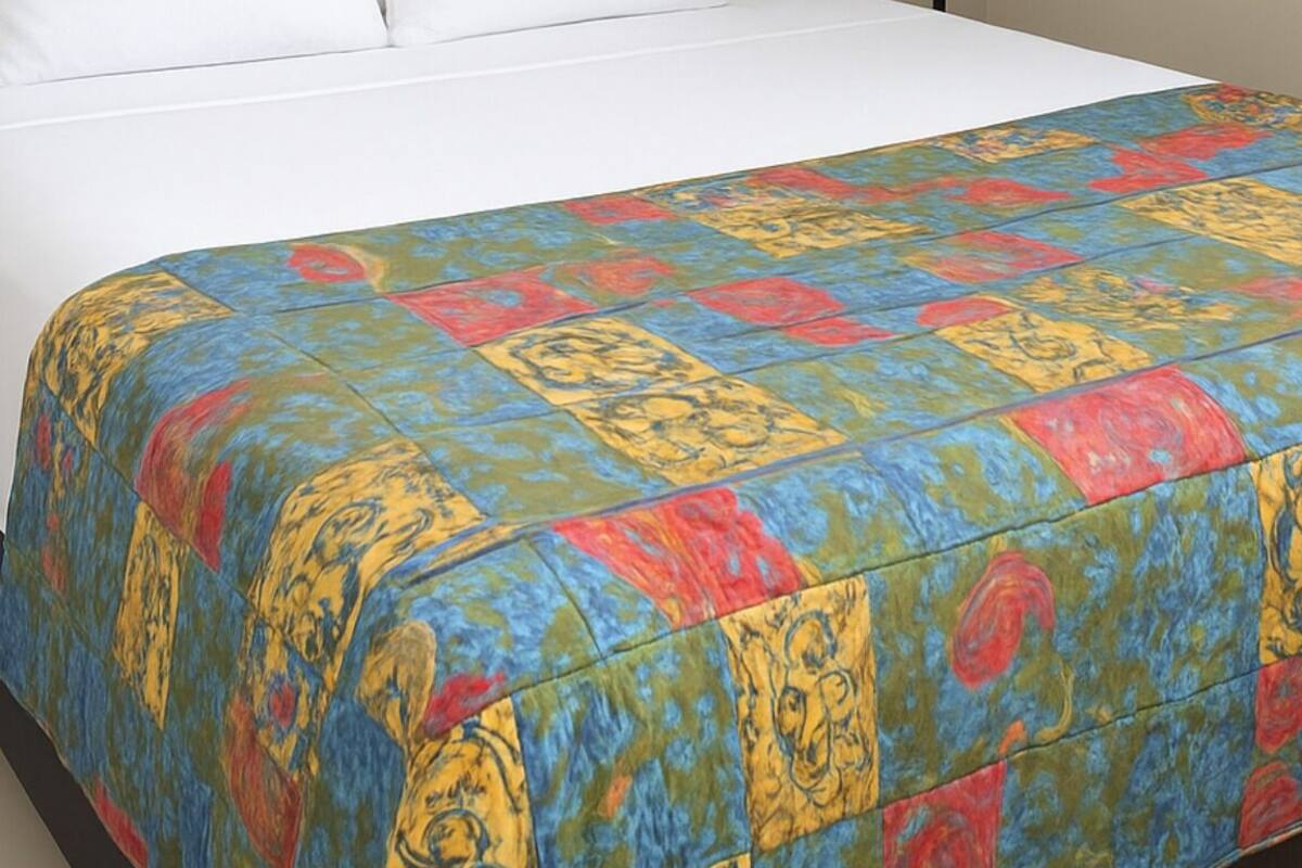 A hotel room with a bed, a colorful quilt, a lamp, and a plain wall.